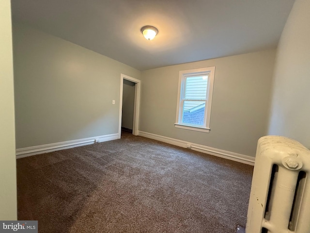 empty room with baseboards, dark carpet, and radiator heating unit