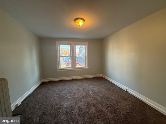 empty room featuring radiator, baseboards, and dark colored carpet