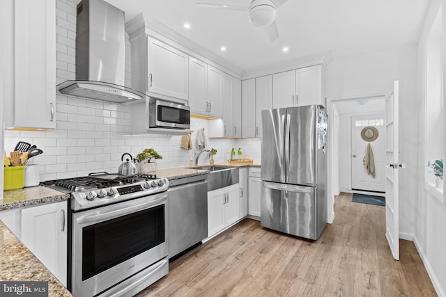 kitchen featuring light wood finished floors, wall chimney range hood, stainless steel appliances, white cabinetry, and a sink