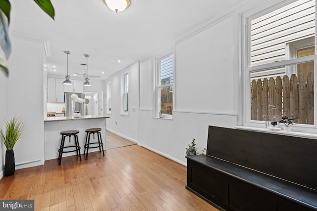 kitchen with pendant lighting, light wood-style flooring, a kitchen breakfast bar, stainless steel refrigerator, and white cabinetry