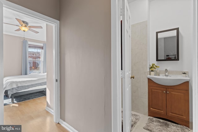 bathroom featuring crown molding, baseboards, wood finished floors, vanity, and a ceiling fan