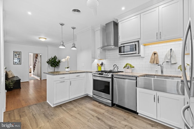 kitchen featuring visible vents, a peninsula, a sink, stainless steel appliances, and wall chimney range hood