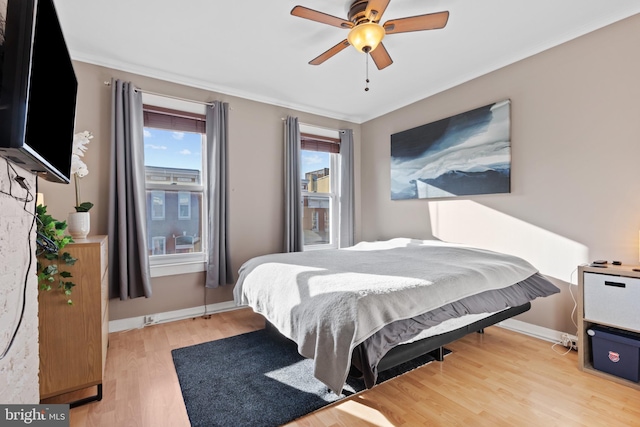 bedroom with crown molding, a ceiling fan, baseboards, and light wood finished floors