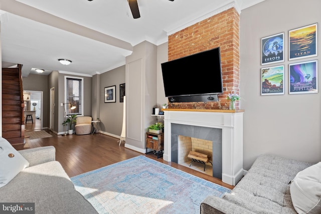 living area featuring ornamental molding, a ceiling fan, a large fireplace, wood-type flooring, and baseboards