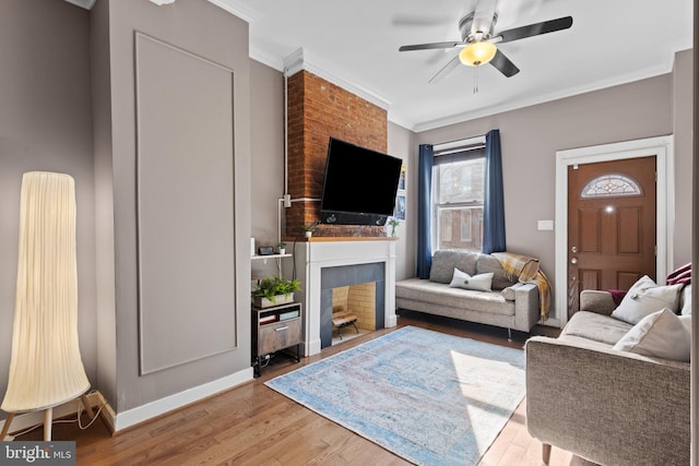 living area with baseboards, ceiling fan, ornamental molding, a fireplace, and wood finished floors