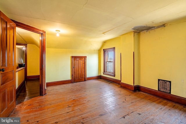 unfurnished room featuring lofted ceiling, baseboards, and wood-type flooring