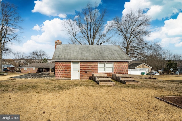 view of front facade featuring brick siding, a chimney, a front yard, and fence