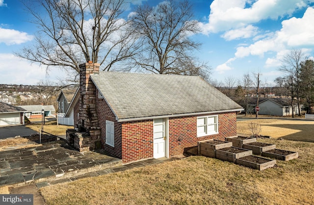 view of side of property with a vegetable garden, brick siding, roof with shingles, and a chimney