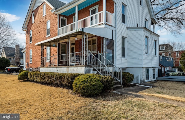 view of front of house with a front yard, stairway, a balcony, covered porch, and brick siding