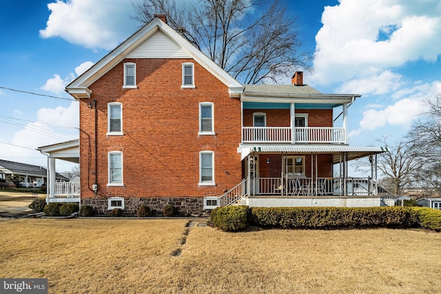 rear view of property featuring a porch, a balcony, brick siding, and a chimney