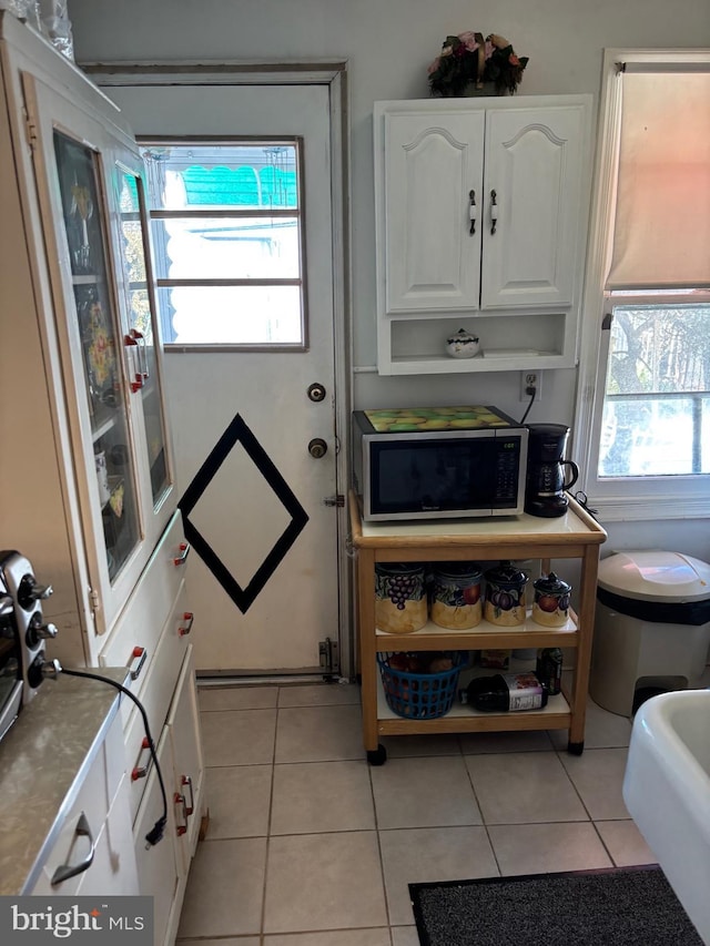 kitchen with light tile patterned floors, stainless steel microwave, open shelves, and white cabinets