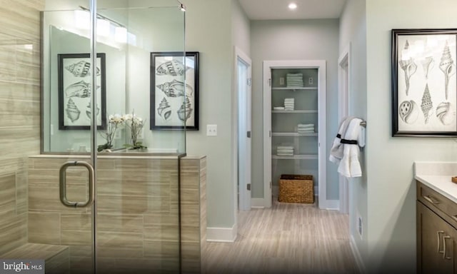 full bath featuring a stall shower, wood finished floors, recessed lighting, baseboards, and vanity