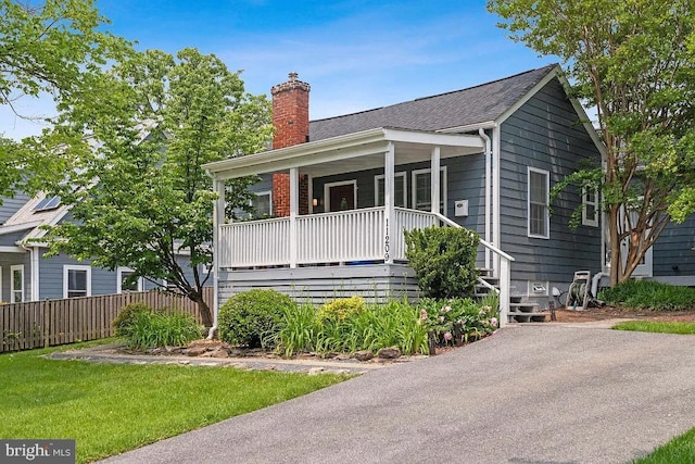 view of front of house with covered porch, a chimney, a front yard, and roof with shingles