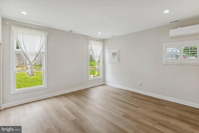 unfurnished room with a wall mounted air conditioner, baseboards, and a wealth of natural light