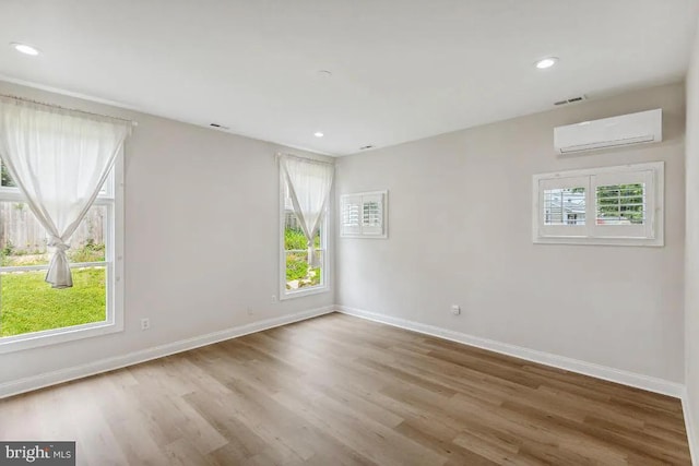 spare room featuring a wall mounted AC, baseboards, and wood finished floors