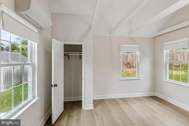 unfurnished bedroom with a wall mounted air conditioner, a closet, baseboards, and light wood finished floors