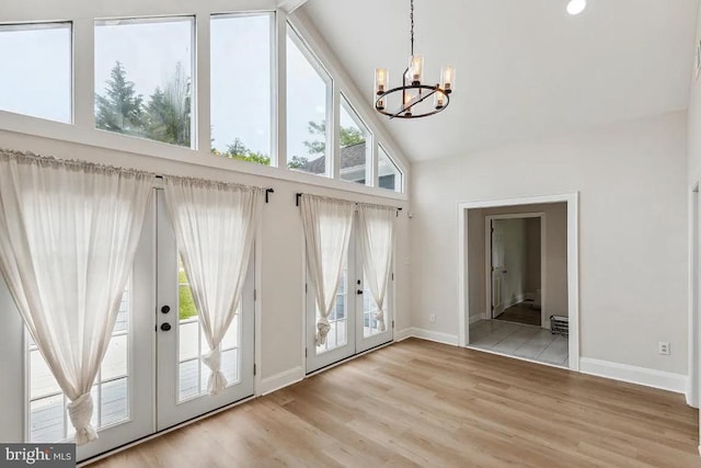 entryway featuring high vaulted ceiling, french doors, light wood finished floors, baseboards, and a chandelier