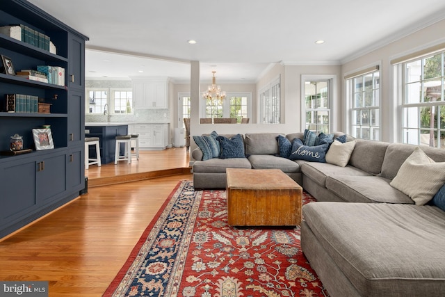 living room with a wealth of natural light, a notable chandelier, light wood finished floors, and ornamental molding