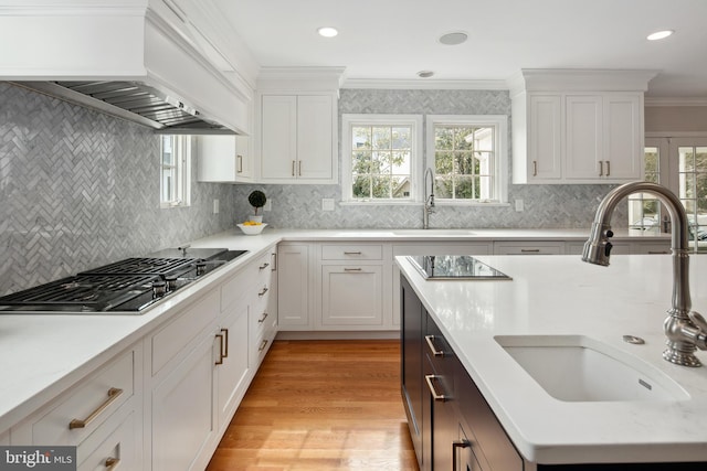 kitchen featuring custom exhaust hood, gas stovetop, black electric cooktop, and a sink