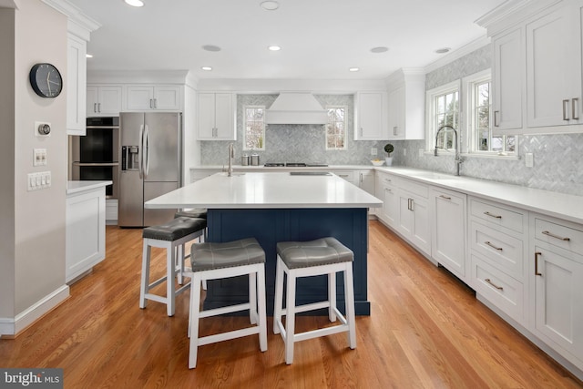 kitchen featuring light wood finished floors, a breakfast bar, appliances with stainless steel finishes, custom exhaust hood, and a sink