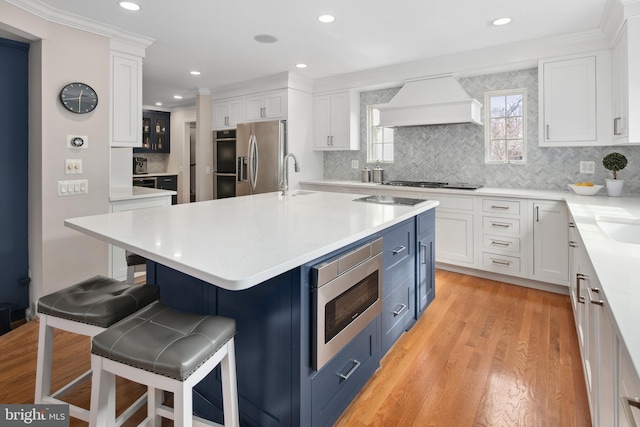 kitchen featuring custom exhaust hood, a sink, stainless steel appliances, white cabinetry, and a kitchen breakfast bar