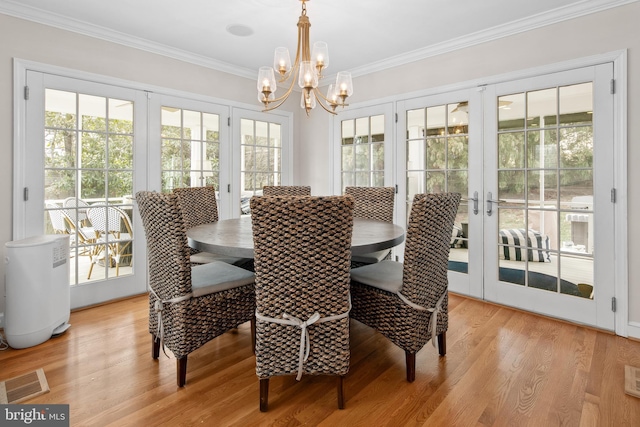 dining space with visible vents, ornamental molding, french doors, light wood-style floors, and a chandelier