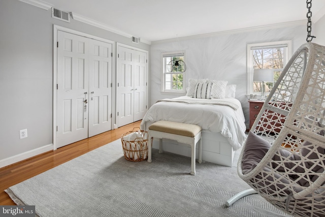 bedroom with visible vents, ornamental molding, two closets, and wood finished floors