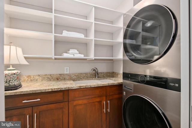 laundry room with cabinet space, stacked washer / drying machine, and a sink