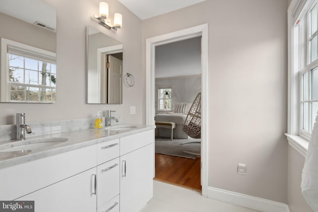 ensuite bathroom with visible vents, connected bathroom, baseboards, and a sink