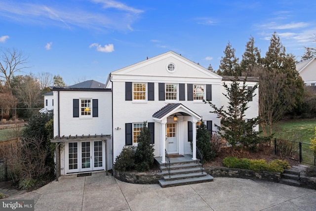 neoclassical / greek revival house with fence, brick siding, and french doors