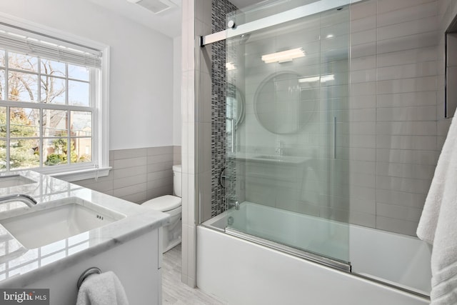 full bath with vanity, visible vents, shower / bath combination with glass door, tile walls, and toilet