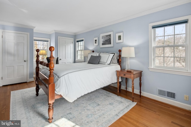 bedroom featuring visible vents, baseboards, wood finished floors, and ornamental molding