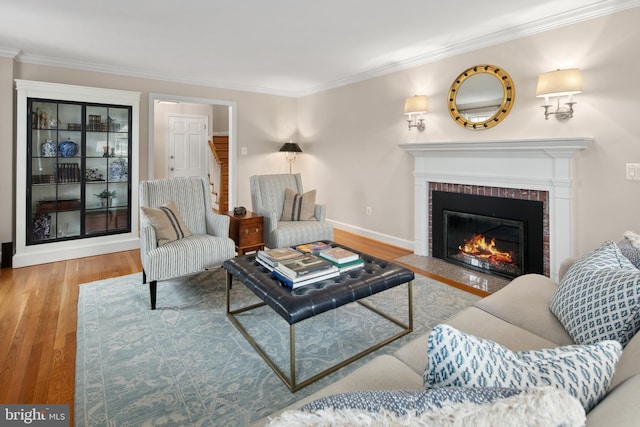 living room with a brick fireplace, crown molding, baseboards, and wood finished floors