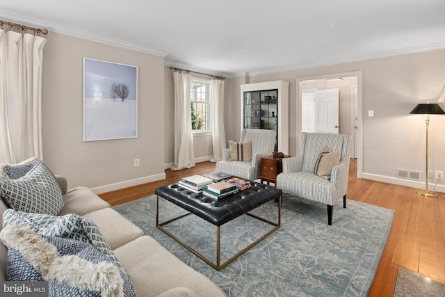 living room featuring crown molding, baseboards, visible vents, and light wood finished floors