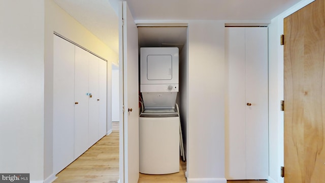 clothes washing area featuring laundry area, light wood-style floors, and stacked washer / drying machine