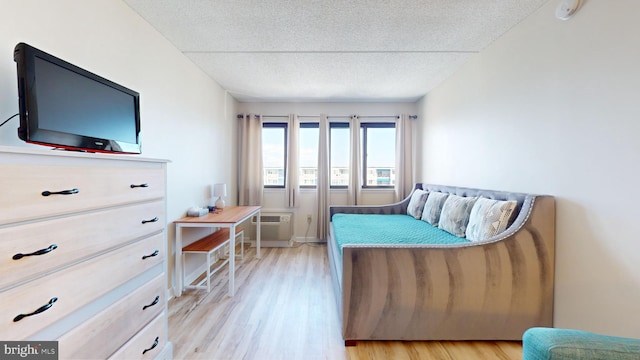 bedroom with a wall mounted AC, a textured ceiling, and light wood-type flooring