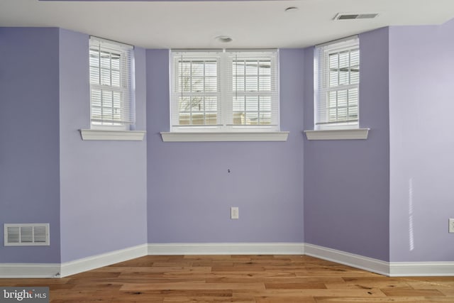 empty room with wood finished floors, visible vents, and baseboards