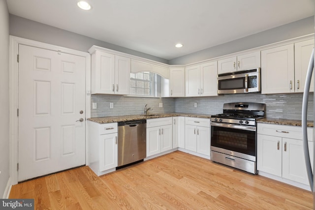 kitchen with light wood-style flooring, a sink, white cabinetry, appliances with stainless steel finishes, and stone counters