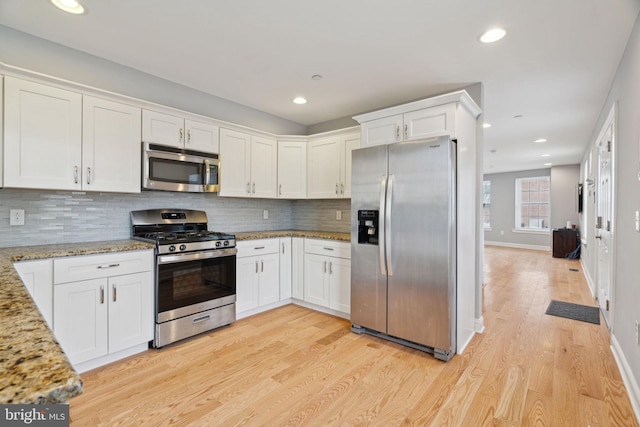 kitchen featuring light wood-style flooring, backsplash, appliances with stainless steel finishes, white cabinets, and light stone countertops