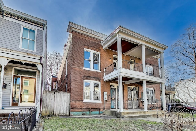 view of front of home featuring brick siding, a balcony, and fence