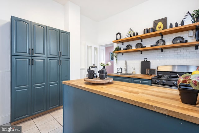 kitchen featuring blue cabinetry, wooden counters, gas range oven, and a sink