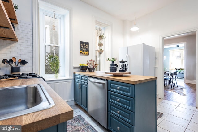 kitchen featuring light tile patterned floors, wooden counters, stainless steel dishwasher, blue cabinets, and backsplash