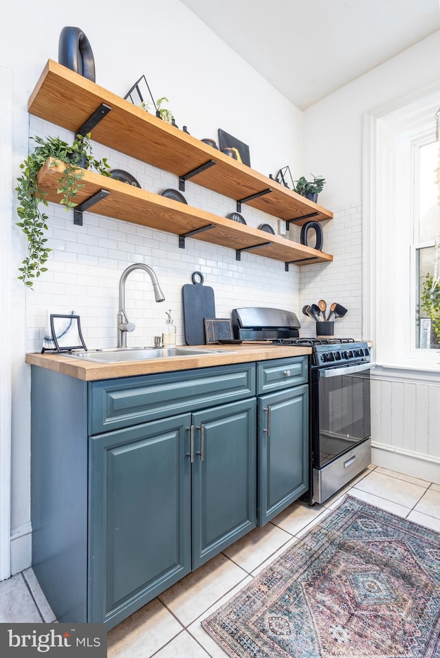 interior space featuring blue cabinetry, open shelves, range with gas cooktop, light tile patterned flooring, and a sink