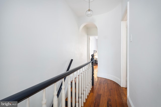 corridor with baseboards, an upstairs landing, arched walkways, and hardwood / wood-style flooring