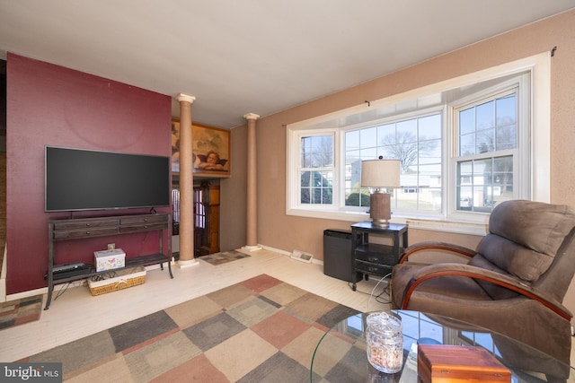 living area with wood finished floors, visible vents, ornate columns, and baseboards