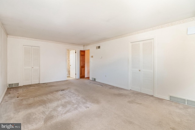 unfurnished bedroom with visible vents, two closets, and carpet floors