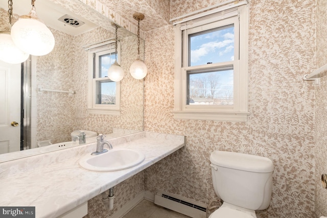 bathroom with a sink, baseboard heating, toilet, and wallpapered walls