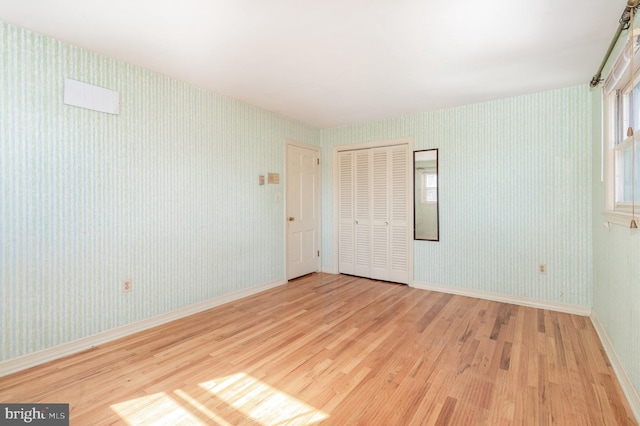 unfurnished bedroom featuring wallpapered walls, wood finished floors, and baseboards