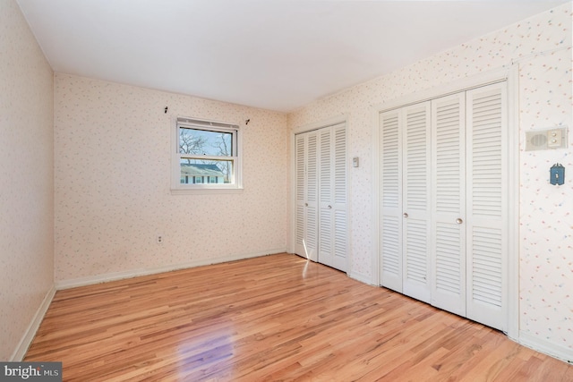 unfurnished bedroom featuring baseboards, two closets, wood finished floors, and wallpapered walls