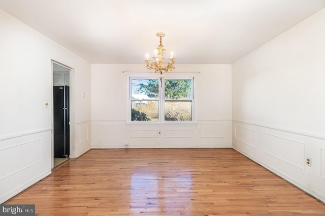 empty room featuring a notable chandelier, wainscoting, and light wood finished floors